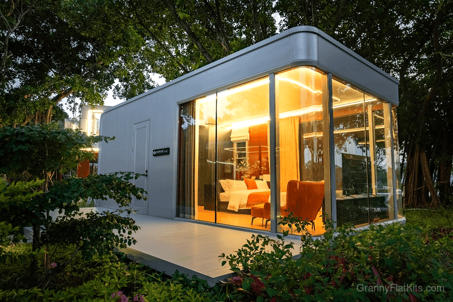 Prefab granny flat kit at dusk with ambient interior lighting and outdoor deck platform